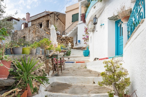 A narrow stone staircase leading to a white building with a blue door, surrounded by potted plants and outdoor furniture.