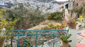 Un balcón con vistas a un pueblo en la ladera, macetas con plantas y un muro de piedra.