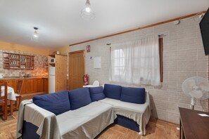 Ein Wohnzimmer mit Ecksofa, Esstisch, Küchenzeile und Backsteinwand.