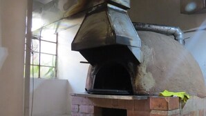 Un horno de pizza al aire libre de ladrillo, con chimenea, ventana y suelo de baldosas.