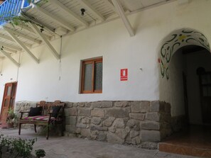 A building with a stone wall, a wooden bench, a window, and an exit sign. - Hab. Family in Beautiful Colonial House in the Center of Cusco / Patio - 4 people (Cusco)
