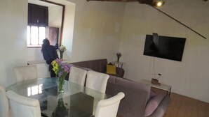 Un comedor con una mesa de vidrio y sillas blancas, un sofá y un televisor montado en la pared.