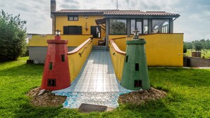 A yellow building with a tiled walkway leading to a door, flanked by two small, colorful lighthouse models. - Villa 'Paradiso' with Private Terrace, Private Garden and Wi-Fi (Castiglione della Pescaia)
