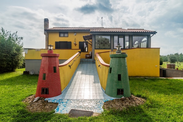 A yellow building with a tiled walkway leading to a door, flanked by two small, colorful lighthouse models.