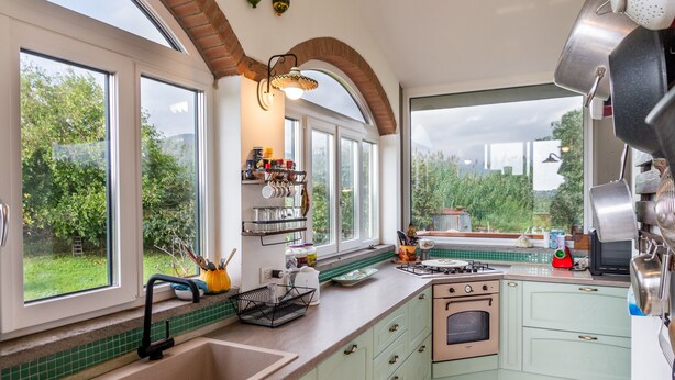 A kitchen with large windows, a sink, a stove, and a countertop with various items. - Villa 'Paradiso' with Private Terrace, Private Garden and Wi-Fi (Castiglione della Pescaia)