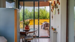 A patio with a table and chairs, a potted plant, and a view of a yellow wall and greenery. - Villa 'Paradiso' with Private Terrace, Private Garden and Wi-Fi (Castiglione della Pescaia)