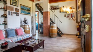A cozy living room with a wooden ceiling, a sofa with colorful cushions, a coffee table with decorative items, and a staircase leading to another room. - Villa 'Paradiso' with Private Terrace, Private Garden and Wi-Fi (Castiglione della Pescaia)