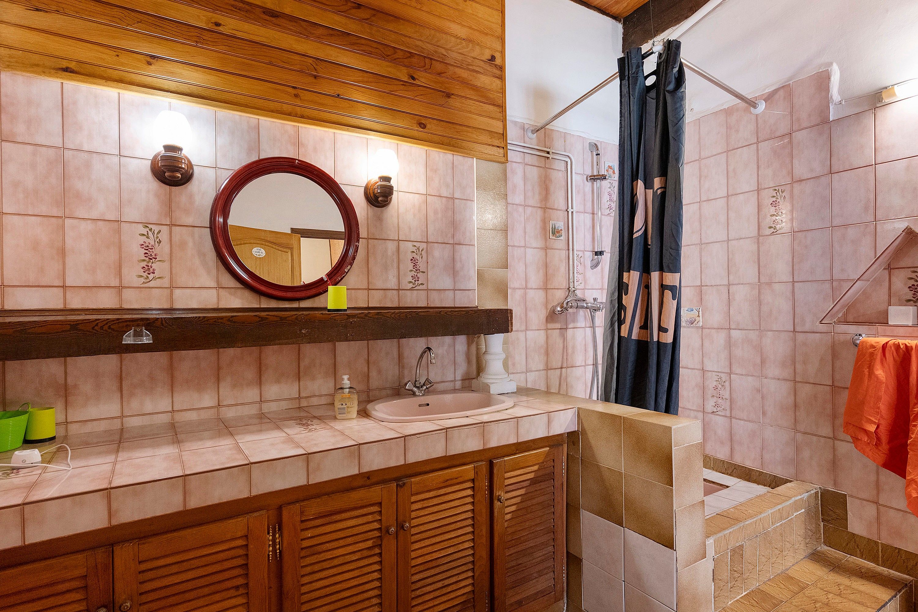 A bathroom with a wooden vanity, a round mirror, a sink, and a shower area.