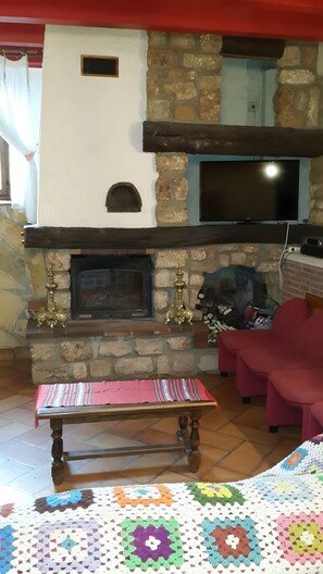 Un salon avec une cheminée en pierre, un téléviseur fixé au-dessus, un banc recouvert d’une nappe à rayures et un plaid en crochet posé sur le sol.