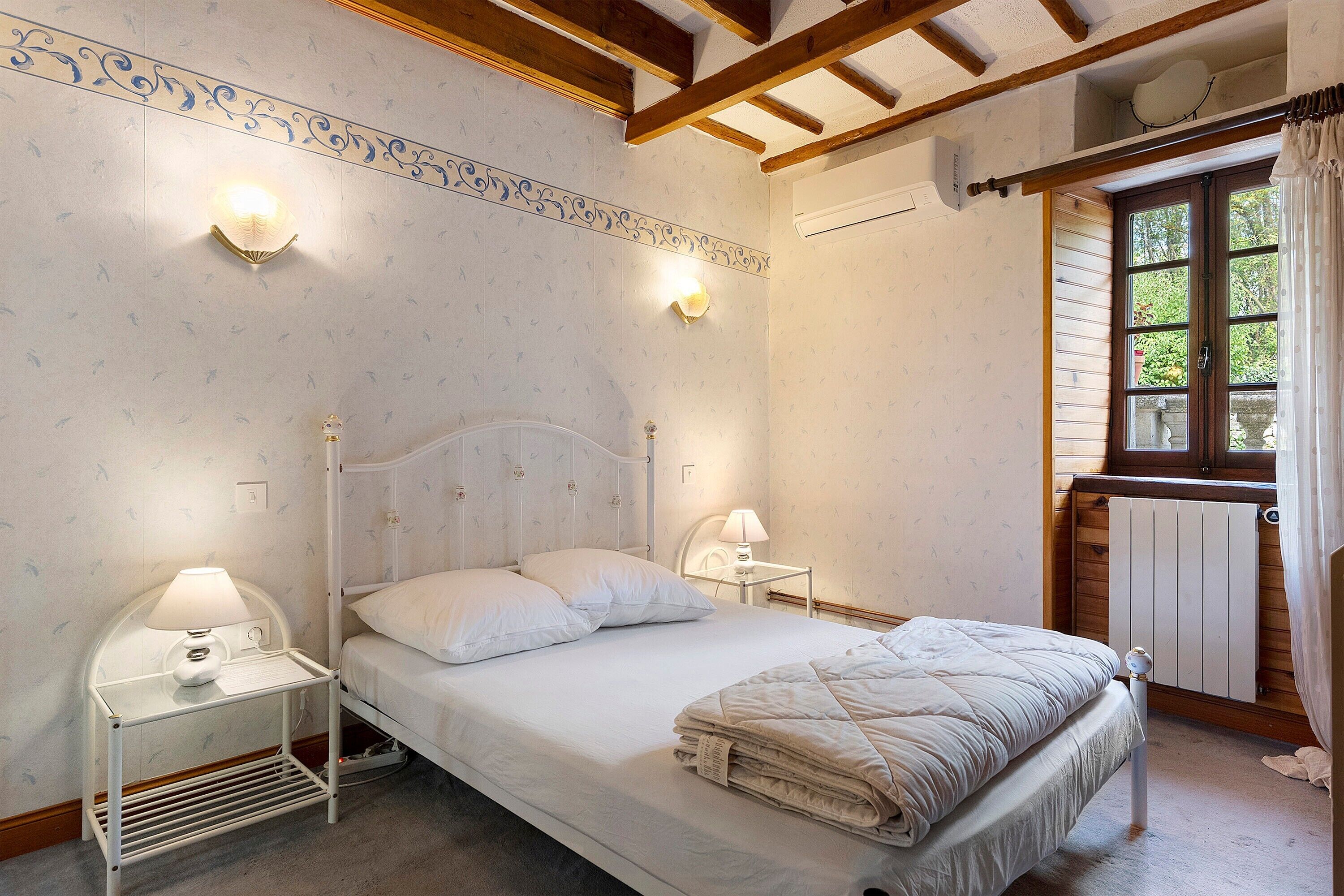 A bedroom with a bed, bedside lamps, a radiator, and a window with curtains.
