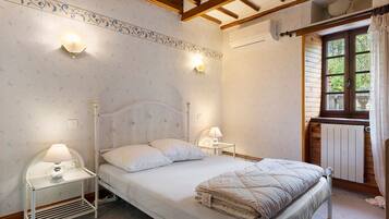A bedroom with a bed, bedside lamps, a radiator, and a window with curtains.