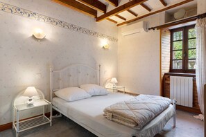 A bedroom with a bed, bedside lamps, a radiator, and a window with curtains.