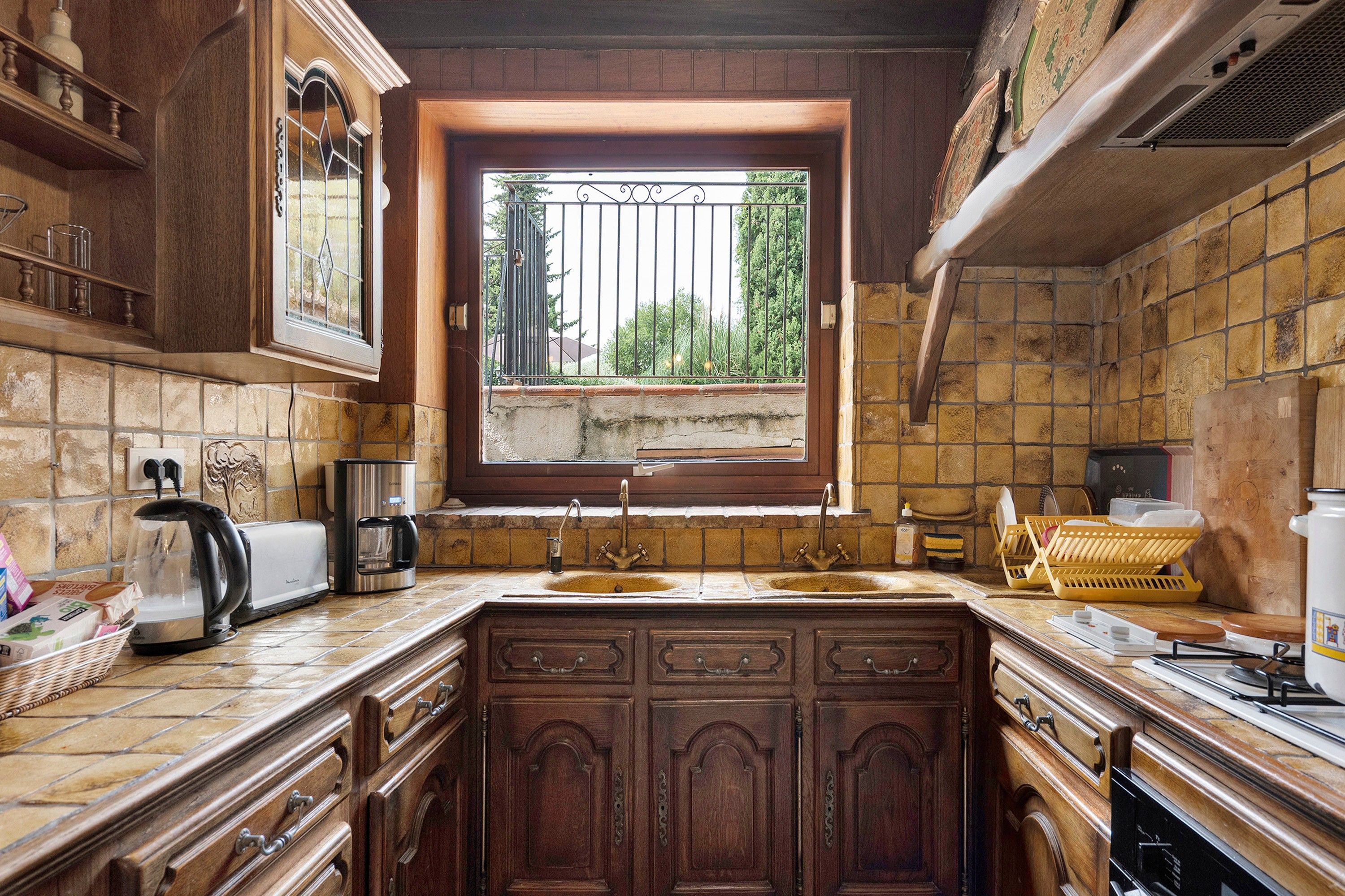 Una cocina con un ventanal grande, armarios de madera, un fregadero y una cafetera.