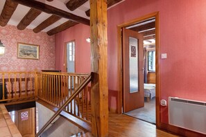 Eine Holztreppe mit Handlauf führt zu einem Zimmer mit einem Bett und einem Heizkörper.
