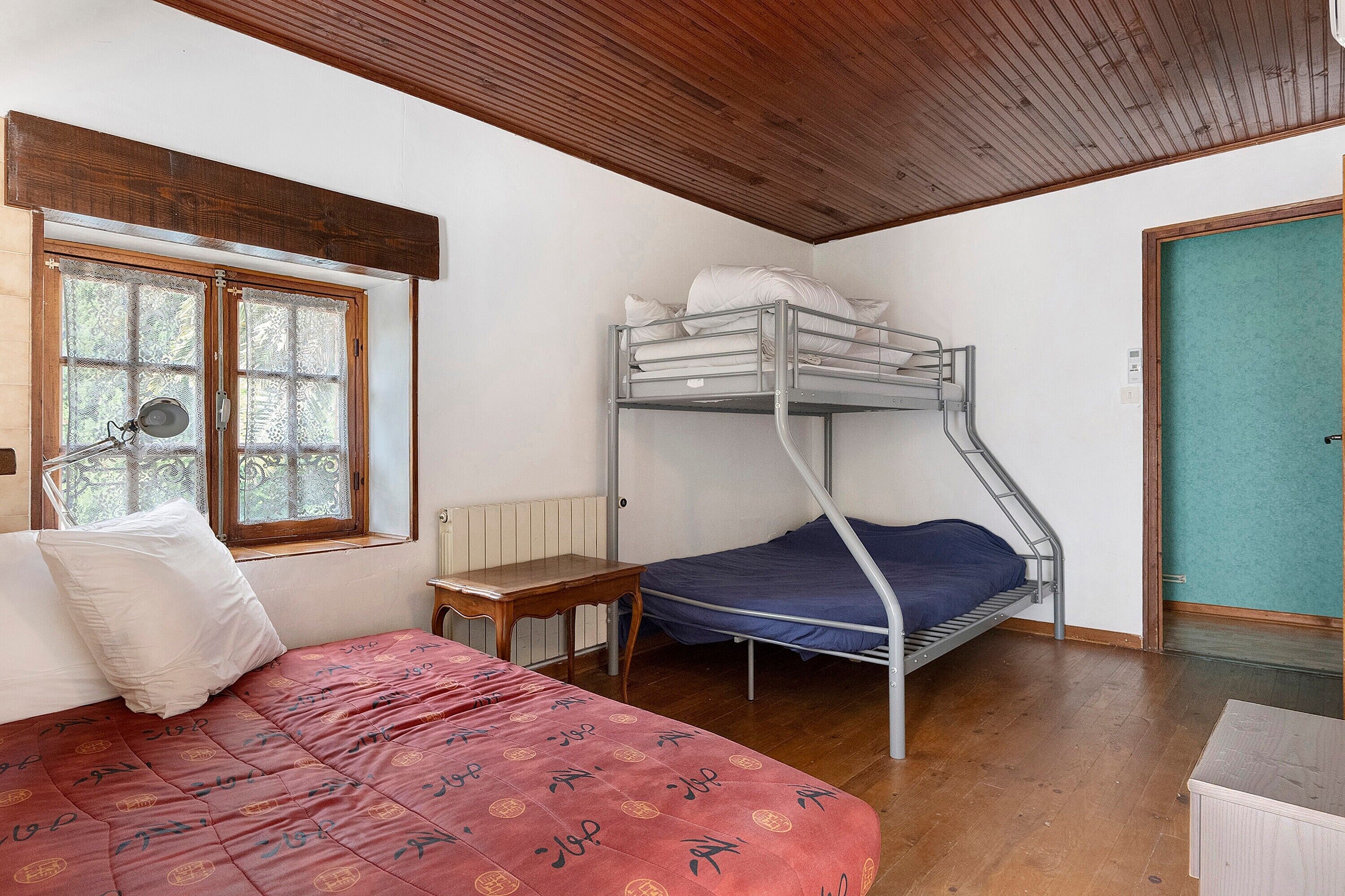 Une chambre avec un lit superposé, un bureau, une fenêtre avec des rideaux en dentelle et un radiateur.