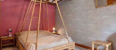 Une chambre avec un lit à baldaquin, une table de chevet avec une lampe, un tabouret en bois et un miroir au mur.