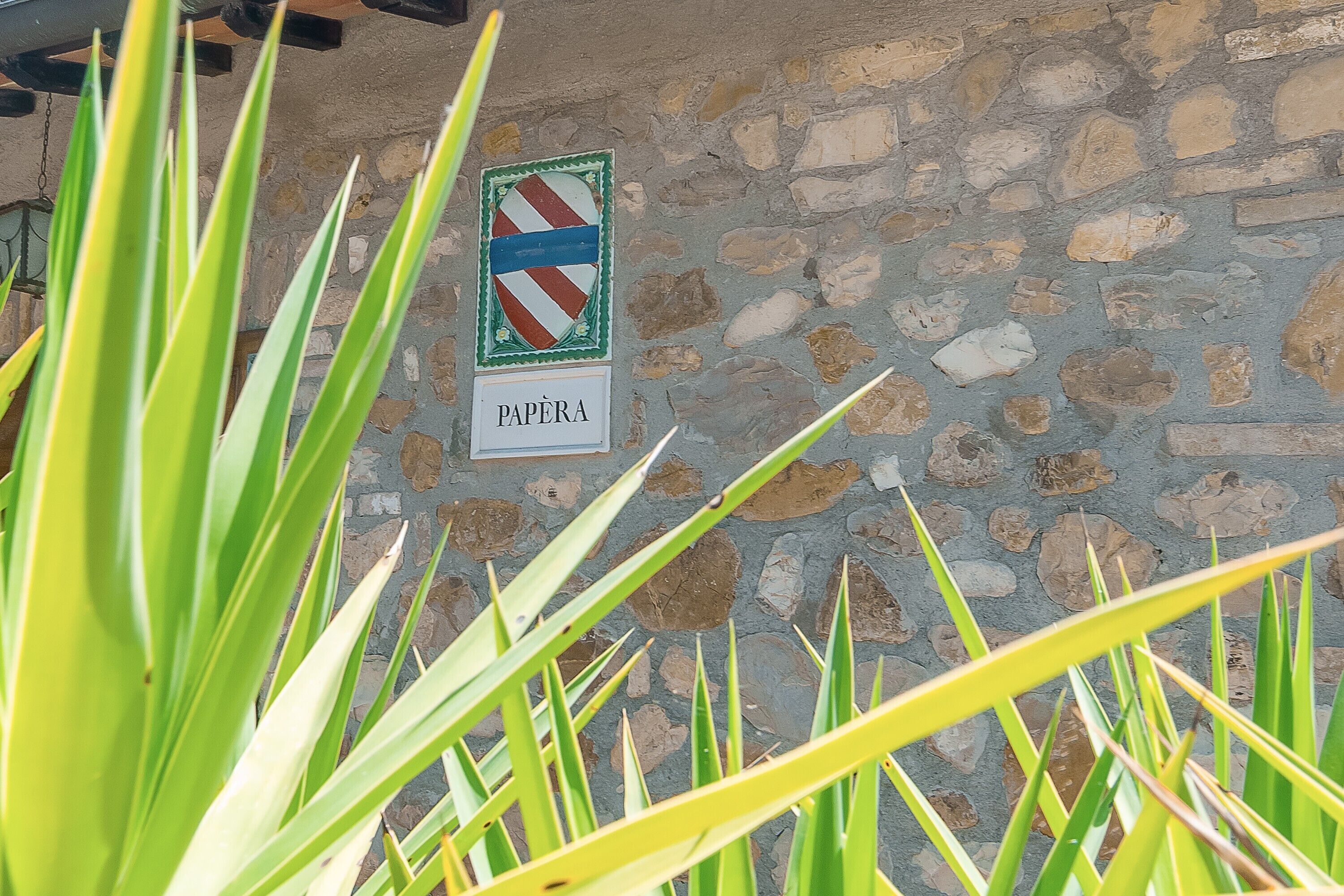 En stenvæg med et skilt der står 'PAPÈRA' og et skjold-emblem.