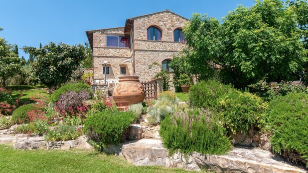 Un bâtiment en pierre doté de nombreuses fenêtres et un jardin où poussent différentes plantes, ainsi qu’un grand pot.