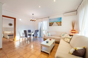 A well-lit living room with a sofa, coffee table, dining area, and a painting on the wall.