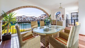 Una mesa con cubierta de vidrio, sillas de mimbre, vista a una piscina y un patio con suelo de ladrillo.