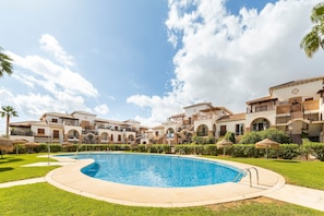 A swimming pool surrounded by a well-maintained lawn, with multi-story buildings in the background.