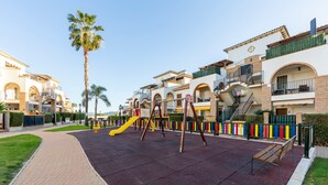 Un parque infantil con un tobogán amarillo, un banco y un sendero pavimentado.