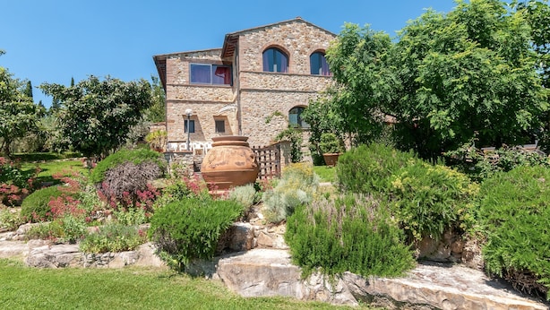 A stone building with multiple windows and a garden with various plants and a large pot. - Podere Papèra - 'Cavallo Flat' Apartment with Mountain View, Wi-Fi and Air Conditioning (San Casciano in Val di Pesa)