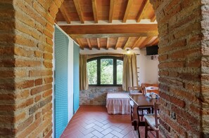 A rustic room with exposed wooden beams, a stone wall, a bed, a table, and a window with curtains.