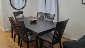 Ruokailutila, jossa on pyöreä pöytä, kuusi tuolia, peili, valkoinen verho ja kuviollinen koristetyyny.