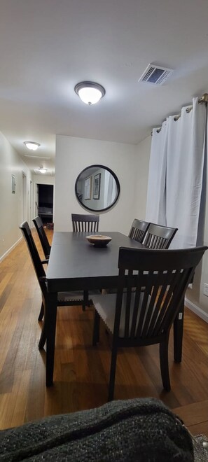 A dining area with a rectangular table, six chairs, a round mirror, and a ceiling light fixture.