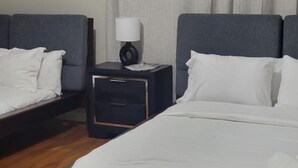 Hotellihuone, jossa on kaksi sänkyä, yöpöytä lampun kanssa, puulattia ja kattovalaisin.