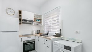 Una cocina compacta con horno integrado, lavadora y ventana con persianas.