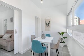 Ett modernt vardagsrum med en soffa, ett matbord med stolar, en krukväxt och ett konstverk som hänger på väggen.