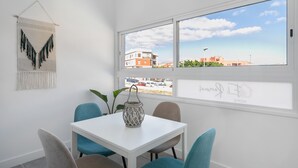 Una habitación con una mesa blanca, sillas color turquesa, un adorno en la pared y vistas de edificios a través de un ventanal grande.