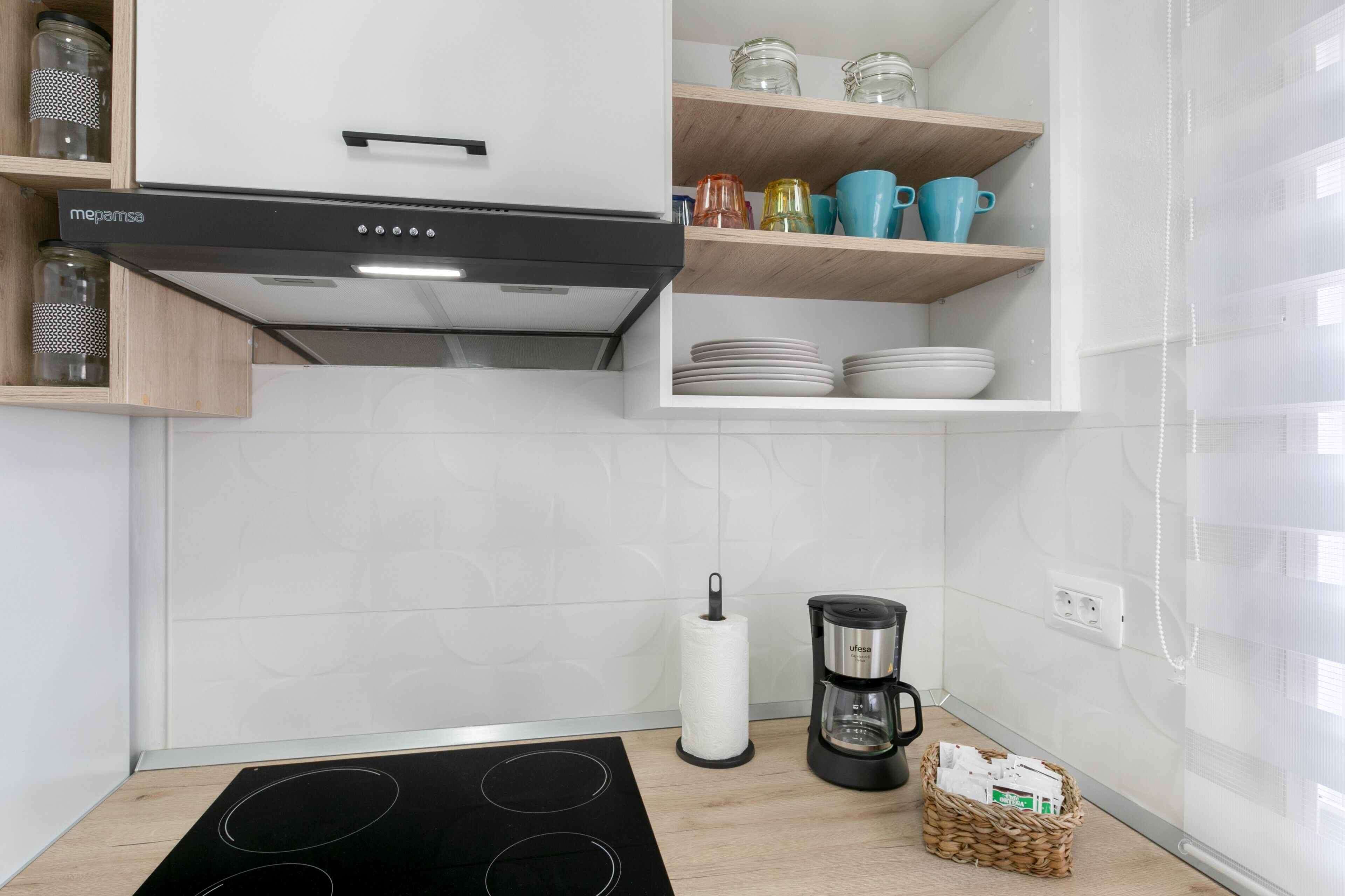 A kitchen with a black stove, a coffee maker, and shelves with dishes and jars.