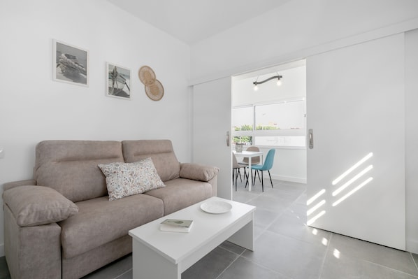 A modern living room with a sofa, a coffee table, and a dining area with chairs and a table.