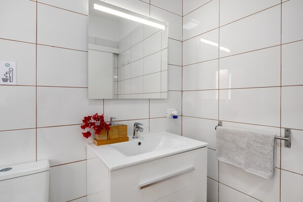 A bathroom with white tiles, a sink, a mirror, a towel rack, and a toilet.