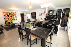 Una cocina moderna con encimeras negras, un comedor con mesa y sillas negras, y un cuadro abstracto de colores en la pared.