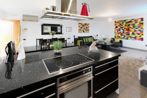 Una cocina moderna con encimera negra, electrodomésticos de acero inoxidable y hervidor rojo.