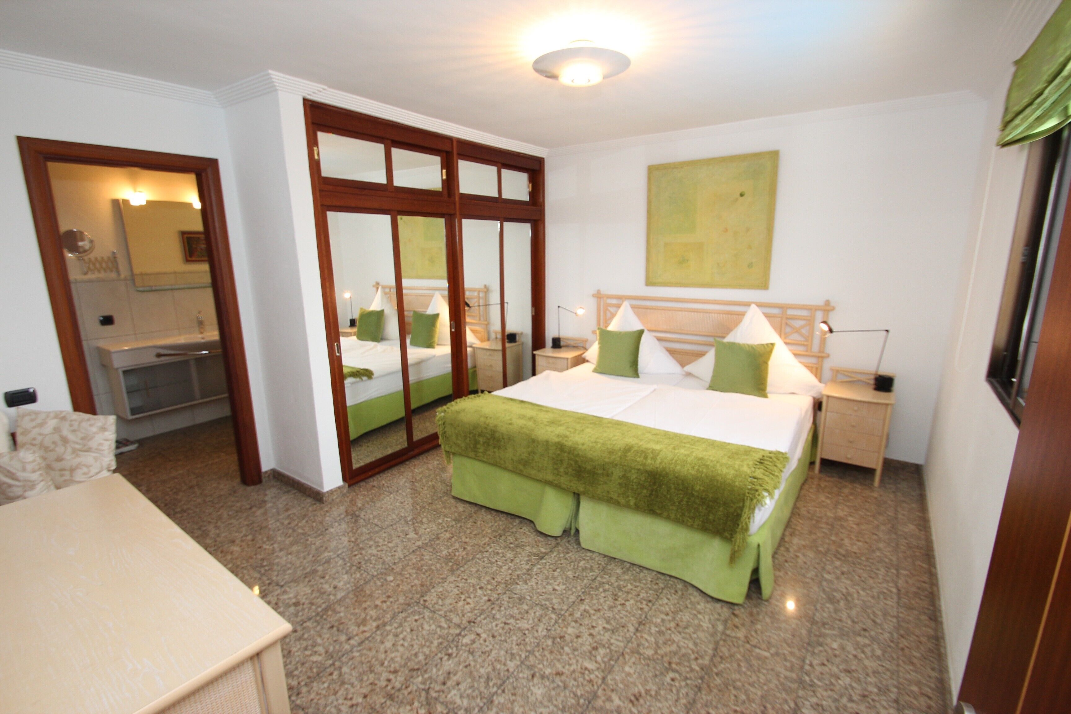 Ein Schlafzimmer mit einem Bett, einem Nachttisch, einem Spiegel und einer Tür mit Glasfeldern.
