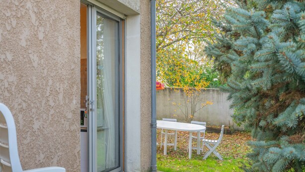 A patio with a white table and chairs, a sliding glass door, and a small tree.