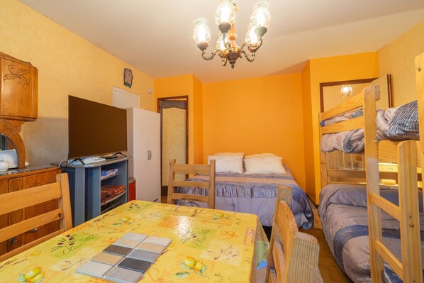 A room with a bunk bed, a desk with a computer, a chair, a table with a tablecloth, and a chandelier.