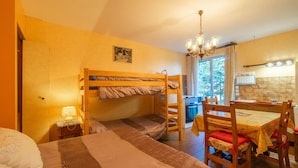 A bunk bed room with a dining table and chairs, a chandelier, and a window with curtains.