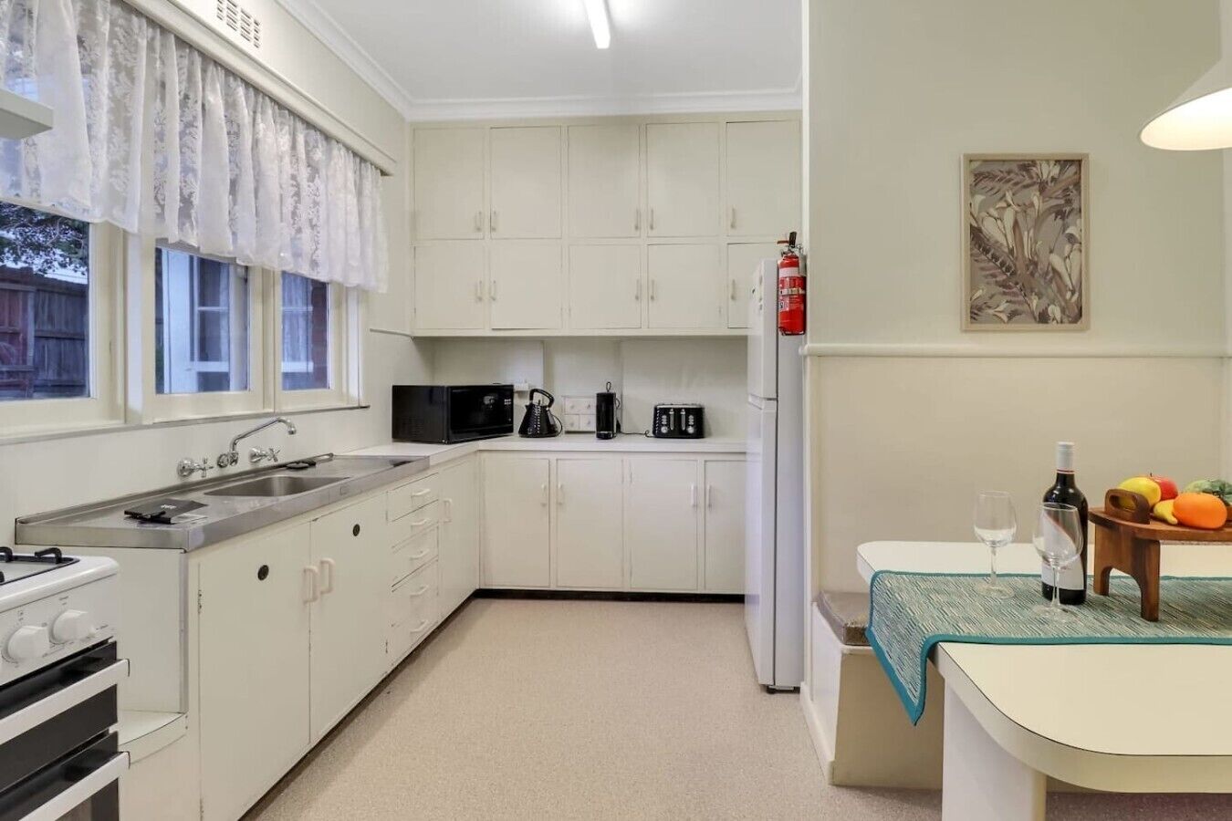 A compact kitchen with white cabinets, a sink, a stove, a microwave, a toaster, and a refrigerator.