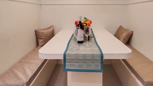 Ein Essbereich mit einem weißen Tisch, einer blauen Tischläufer und einer Obstschale mit Weingläsern.