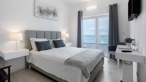 Ein modernes Hotelzimmer mit einem großen Bett, Nachttischen, einem Schreibtisch und Meerblick.