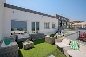 Une terrasse sur le toit avec des sièges extérieurs, une balustrade en verre et une vue sur le paysage environnant.
