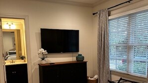 Una camera da letto con un letto, una ventola a soffitto, una televisione, una cassettiera e una finestra con persiane.