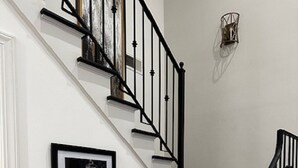 Una scala con ringhiere nere e pareti bianche, un quadro appeso al muro e un lampadario sopra le scale.