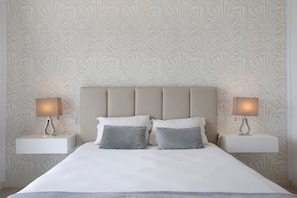 Un lit avec une tête de lit, deux tables de chevet avec des lampes et un papier peint à motifs.